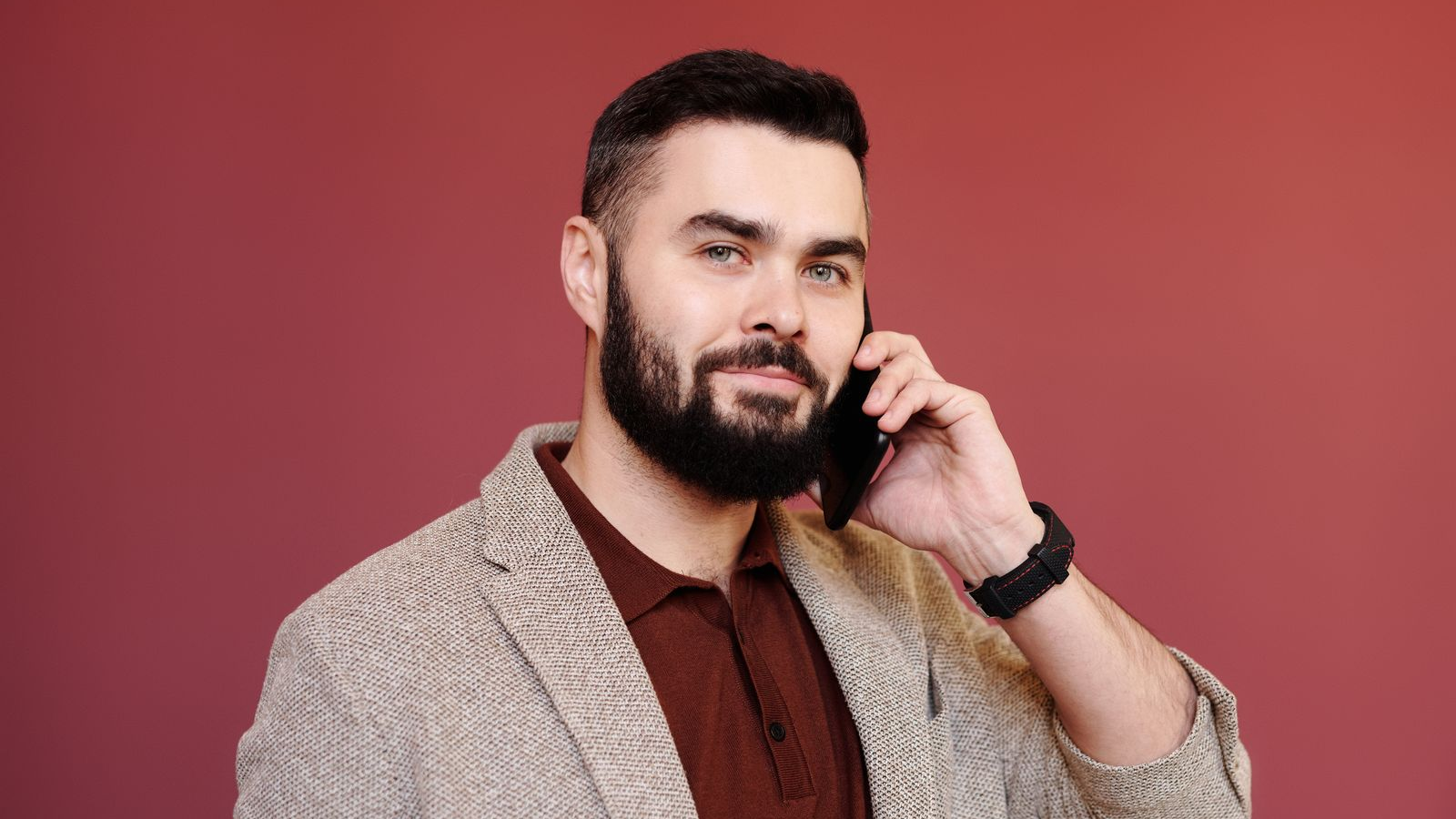 Bearded professional holding a smartphone to his ear during a call in an indoor setting.