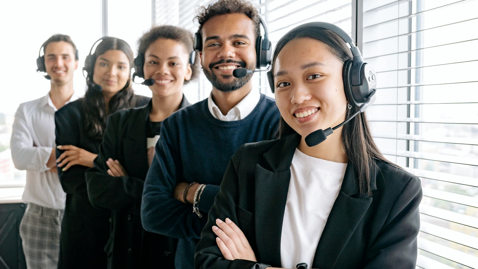 Diverse contact-center agents standing together in an office, each wearing professional over-ear headsets with boom mics, facing the camera.