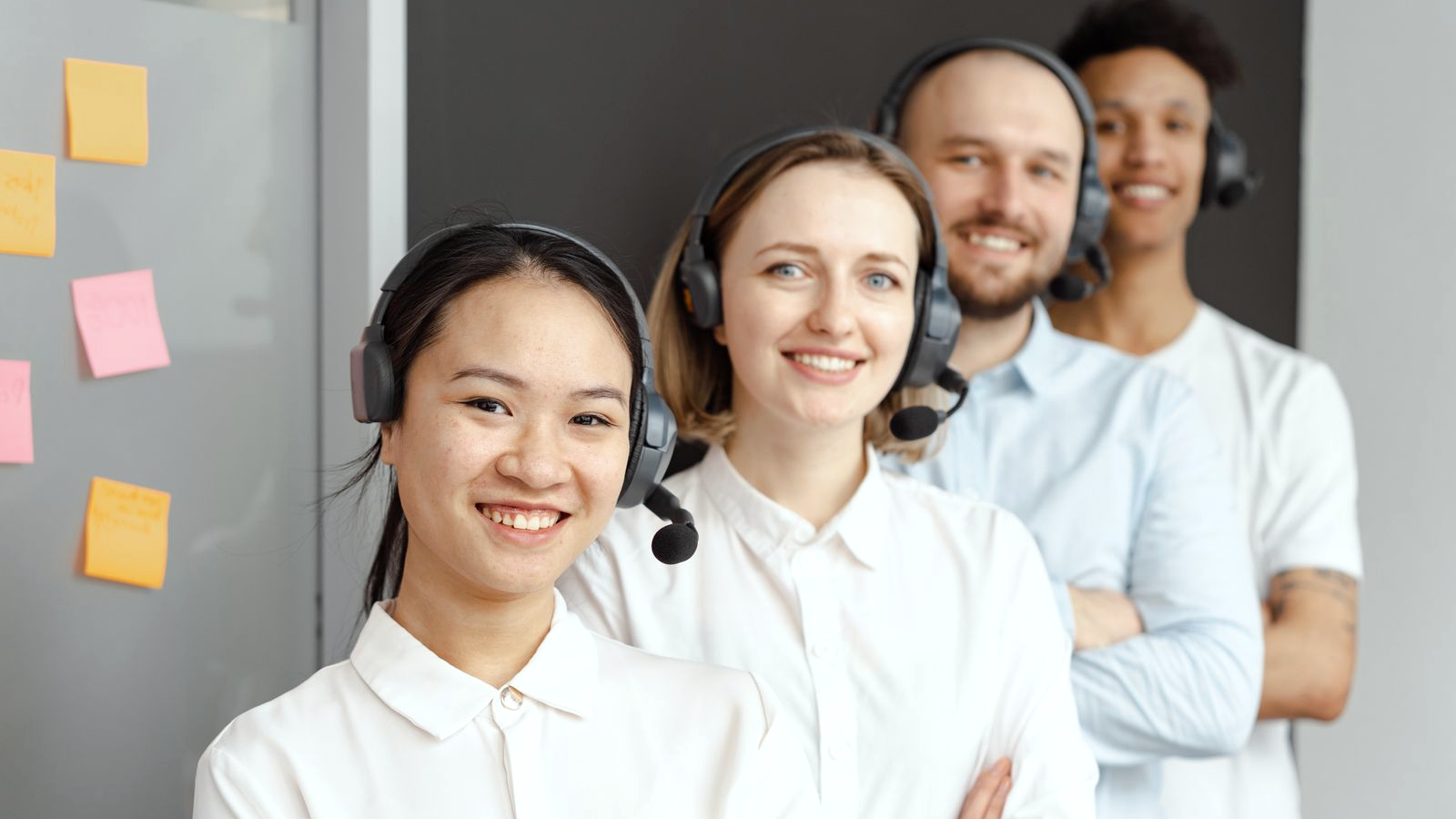 Collections-floor contact-center team wearing headsets, human faces on a shared floor, smiling and ready for the next break-adjacent dial.