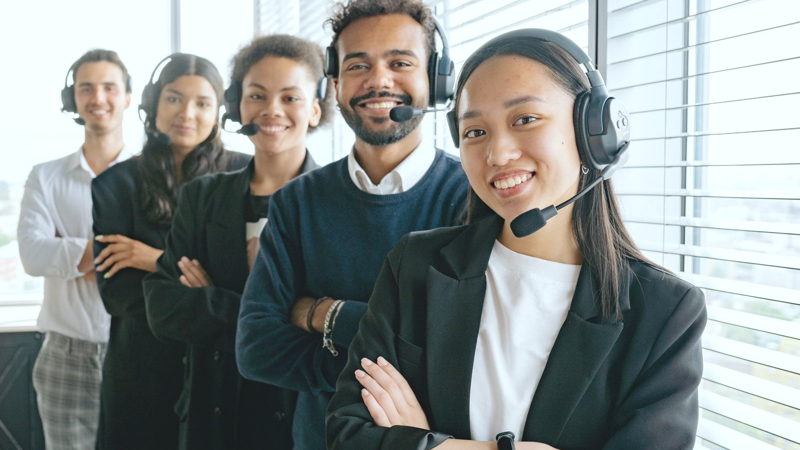 Collections-floor contact-center team wearing headsets, human faces on a shared floor, smiling and ready for the next opening hello.