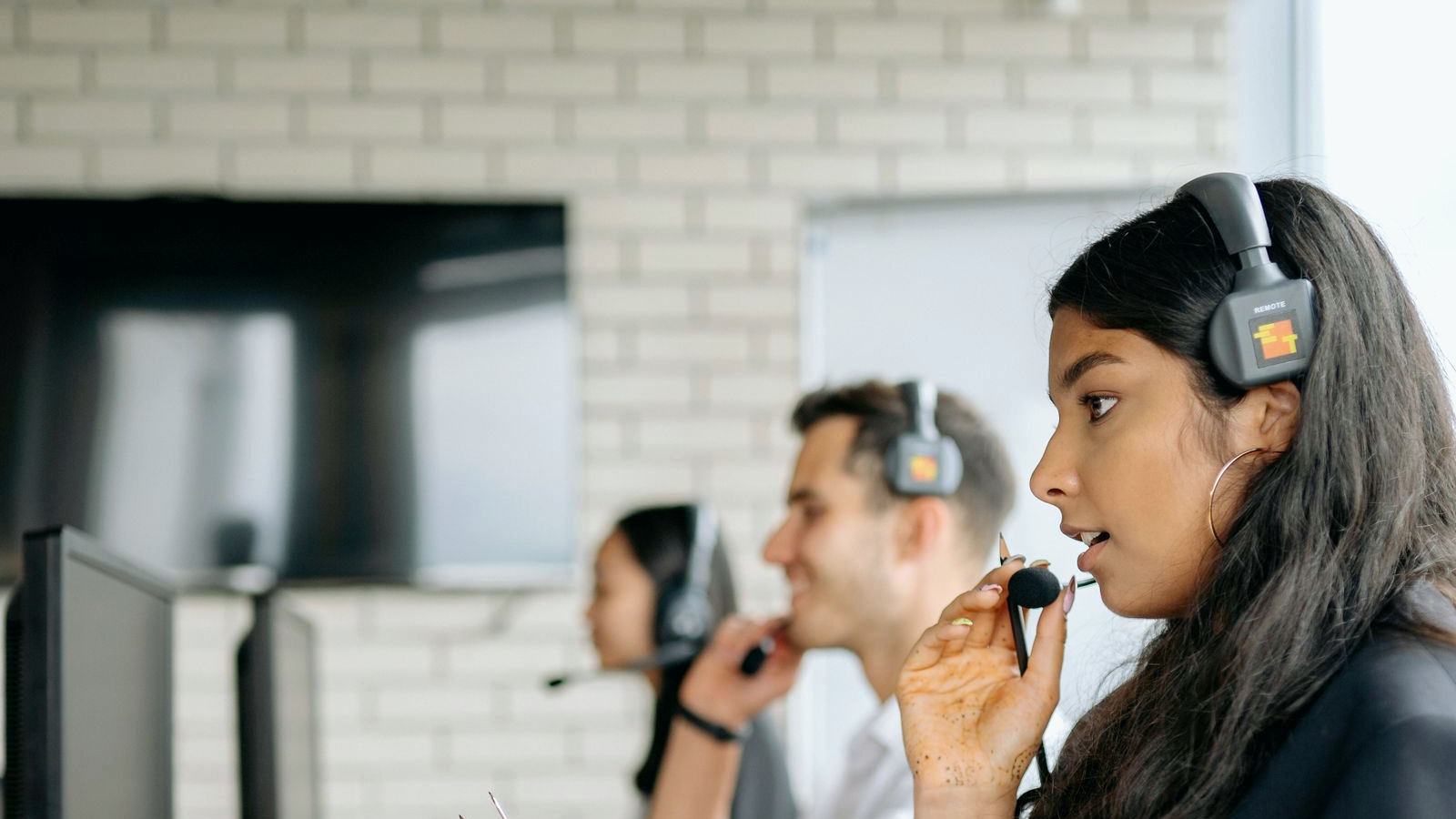 Contact-center professional with a headset on a live floor, human face visible in profile mid-call, colleagues with headsets at desks behind; real collections or call-center environment.