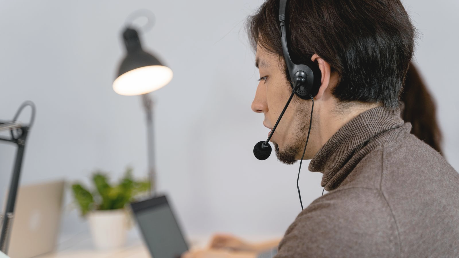 Contact-center agent wearing a headset at a desk, speaking mid-call in a bright modern office.