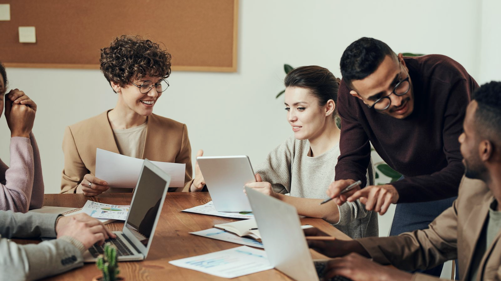 Diverse professionals collaborating around a desk with laptops and charts in a bright office, a coaching and desk scene for sales performance coaches.
