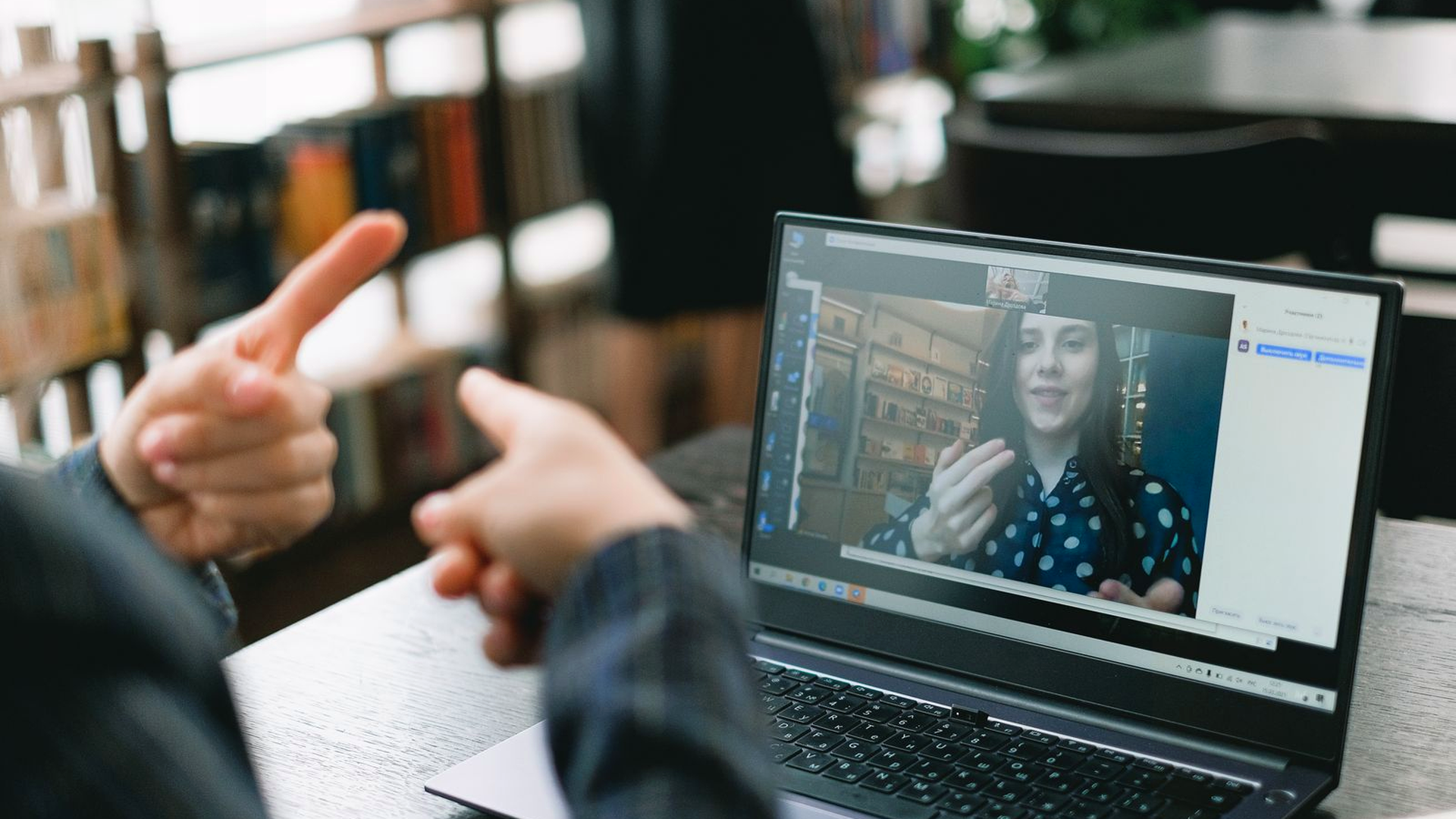 Coach on a laptop video call in a real desk environment with bookshelves behind the screen; human face visible while speaking, photographic stock for end-of-phrase delivery under live coaching pressure.